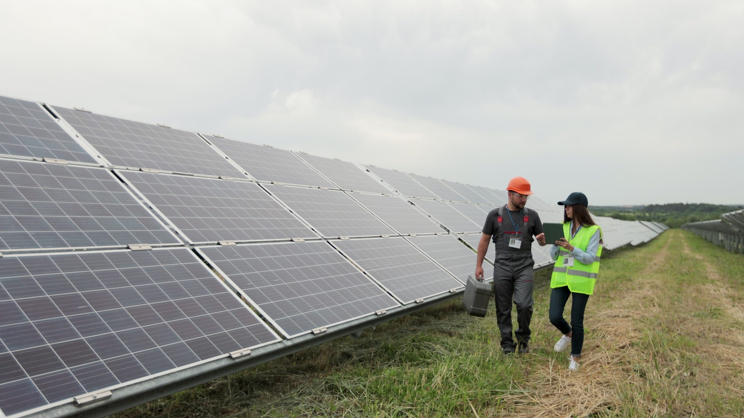Man engineer specialist and female electrical worker walking on photovoltaic solar panels and discussing future plans. Eco-friendly station for renewable energy. Concept of green energy