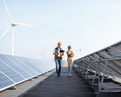 View on the rooftop solar power plant with two engineers walking and examining photovoltaic panels. Concept of alternative energy and its service