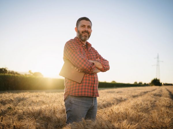 Portrait of a mid-aged modern farmer standing with arms crossed in the wheat field at sunset