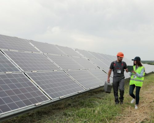 Man engineer specialist and female electrical worker walking on photovoltaic solar panels and discussing future plans. Eco-friendly station for renewable energy. Concept of green energy